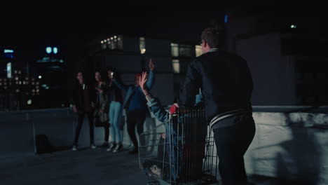 happy group of friends playing with shopping cart having fun on rooftop at night enjoying weekend celebration party