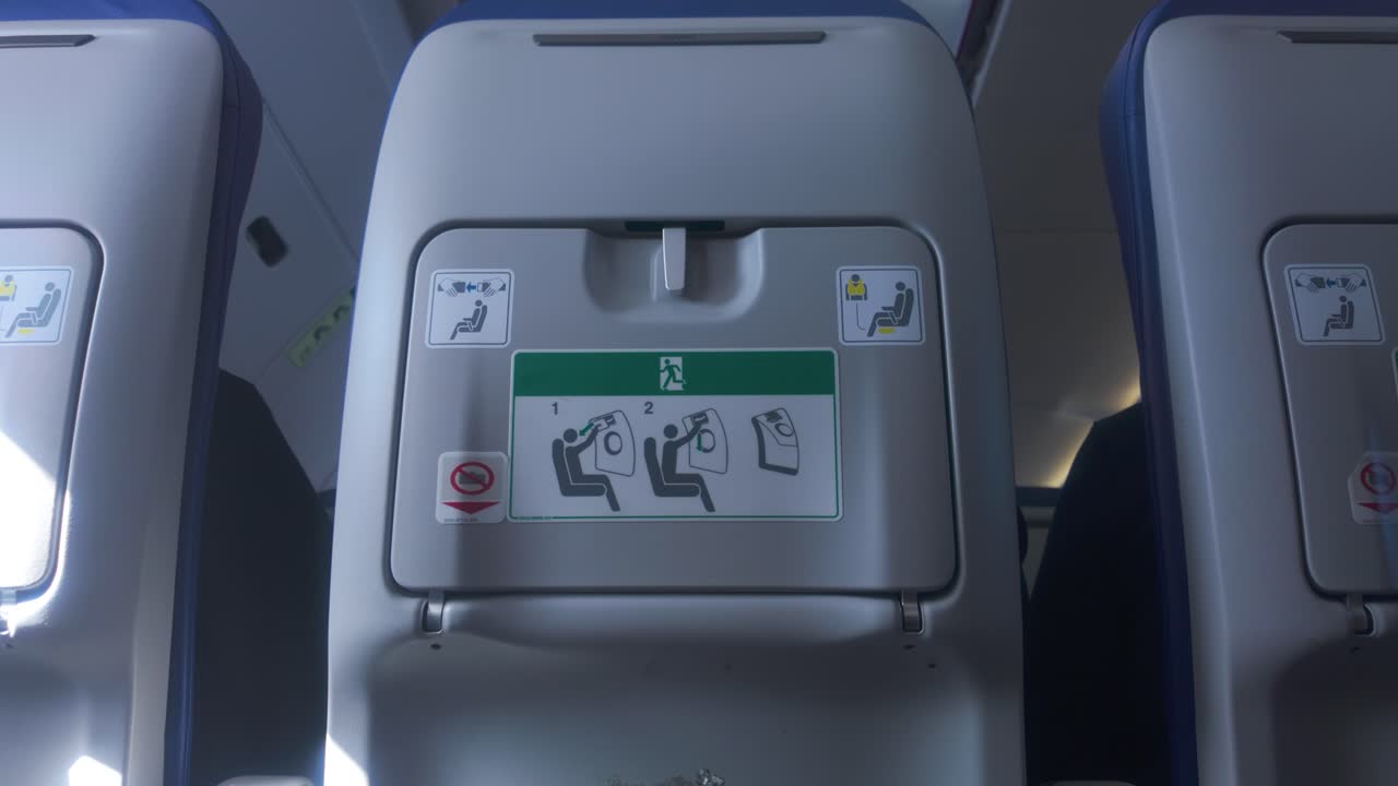 Un braccio tira giù il tavolino pieghevole dal retro del sedile dell'aereo in un'inquadratura media, rivelando il meccanismo pieghevole del piano del tavolino