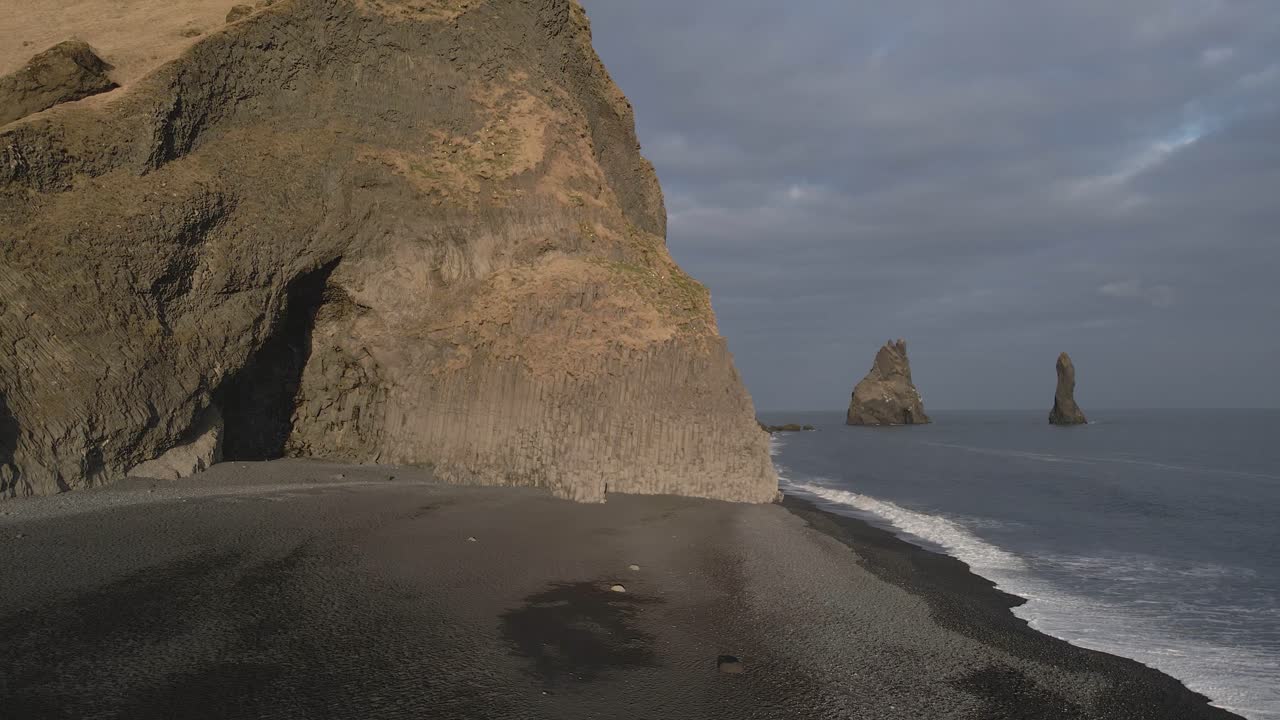 playa de arena negra de reynisfjara con acantilados de basalto y pilas en el fondo, islandia