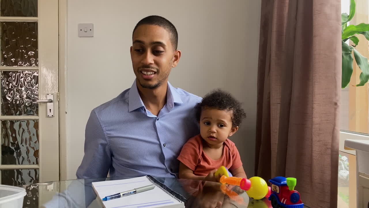 Young Man with Small Child On Business Video Call Listening Intently Whilst Looking Directly to Camera