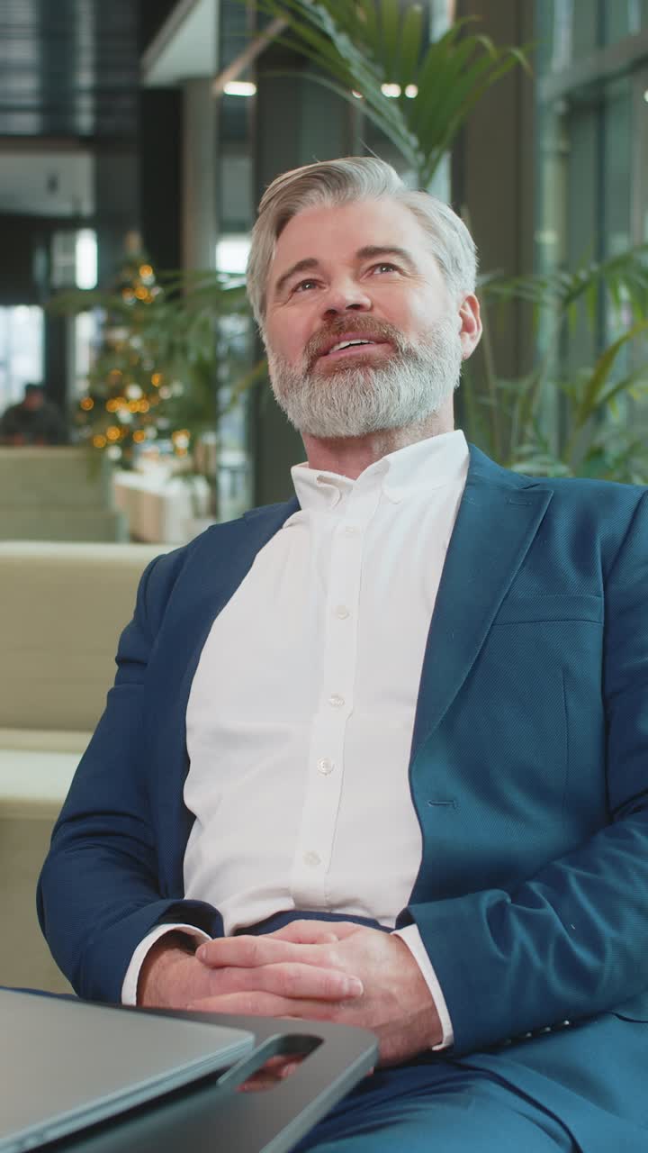 Hombre de negocios feliz sentado en el vestíbulo de la oficina cerrando la computadora portátil y estirando los brazos después de terminar el trabajo