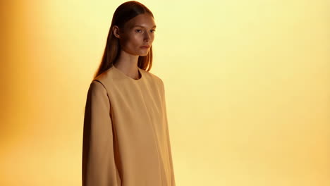 a woman in a beige garment against a warm yellow background