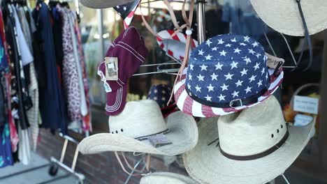 variety of cowboy hats and american themed hats on a rack outside of a thrift store