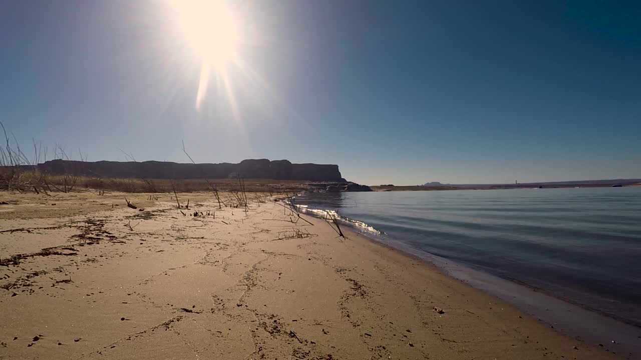 밝은 태양과 사암 버트는 애리조나 페이지 파웰 호수의 황량한 모래 해안을 씻는 파도의 배경입니다.