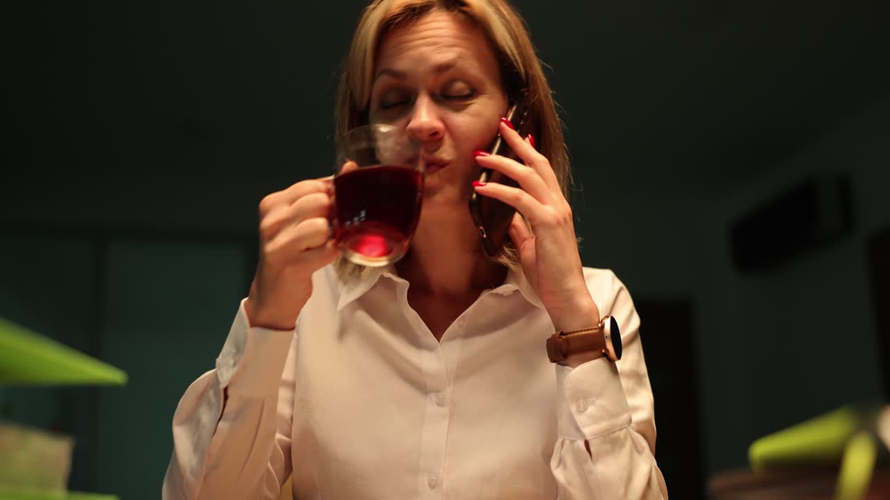 Woman working late, talking on phone and drinking from a mug