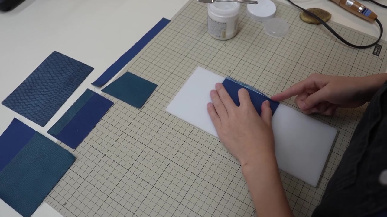 Craftsperson aligns leather rectangles with white card template on mat