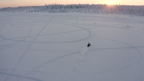 drone shot of a snowmobile on an open snow area in the woods during a cold winter season in sweden