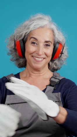 smiling mature woman in work overalls with ear protection and gloves