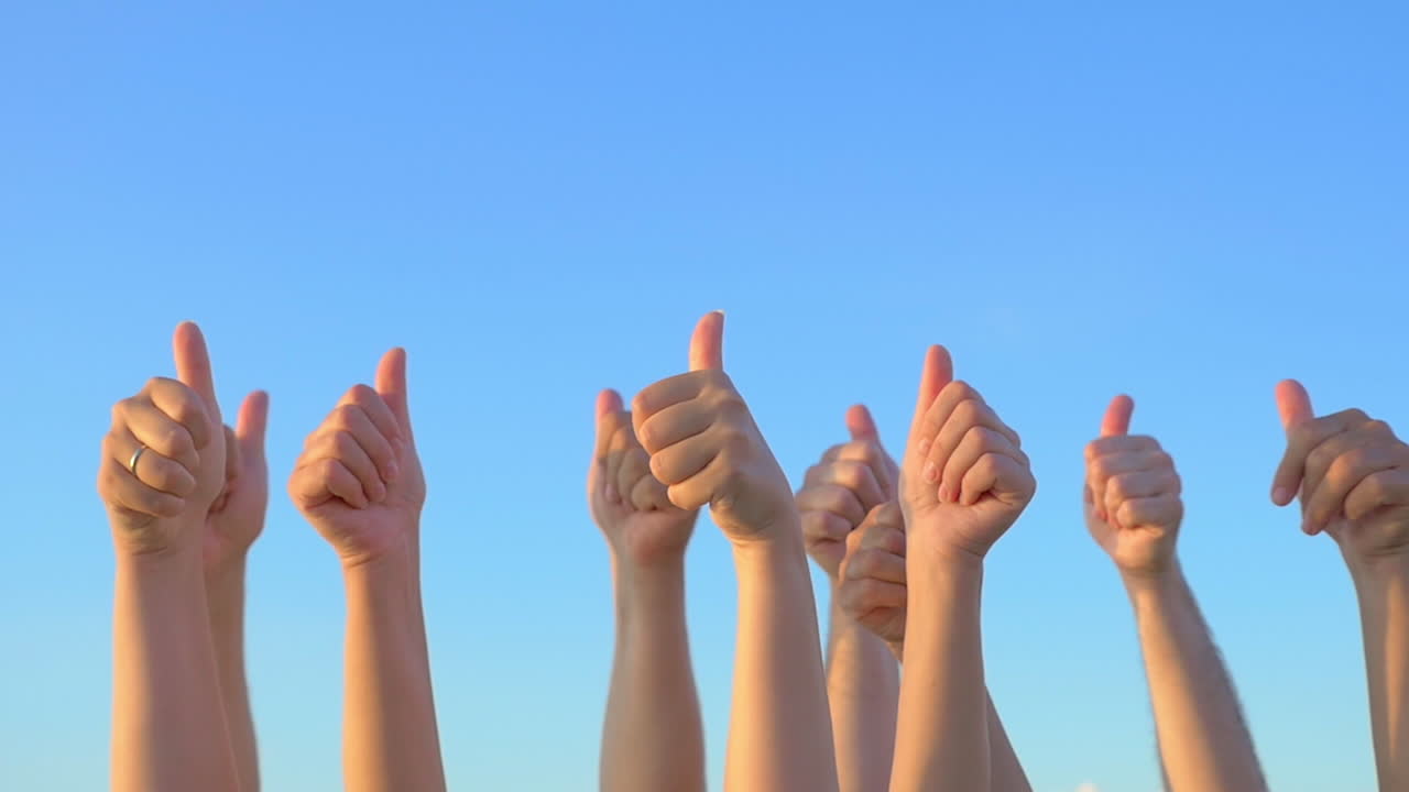 manos arriba con los pulgares hacia arriba contra el cielo azul