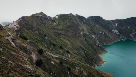 Aerial-view-of-the-mountain-slopes-with-a-blue-lagoon-in-Lake-Quilotoa,-Ecuador