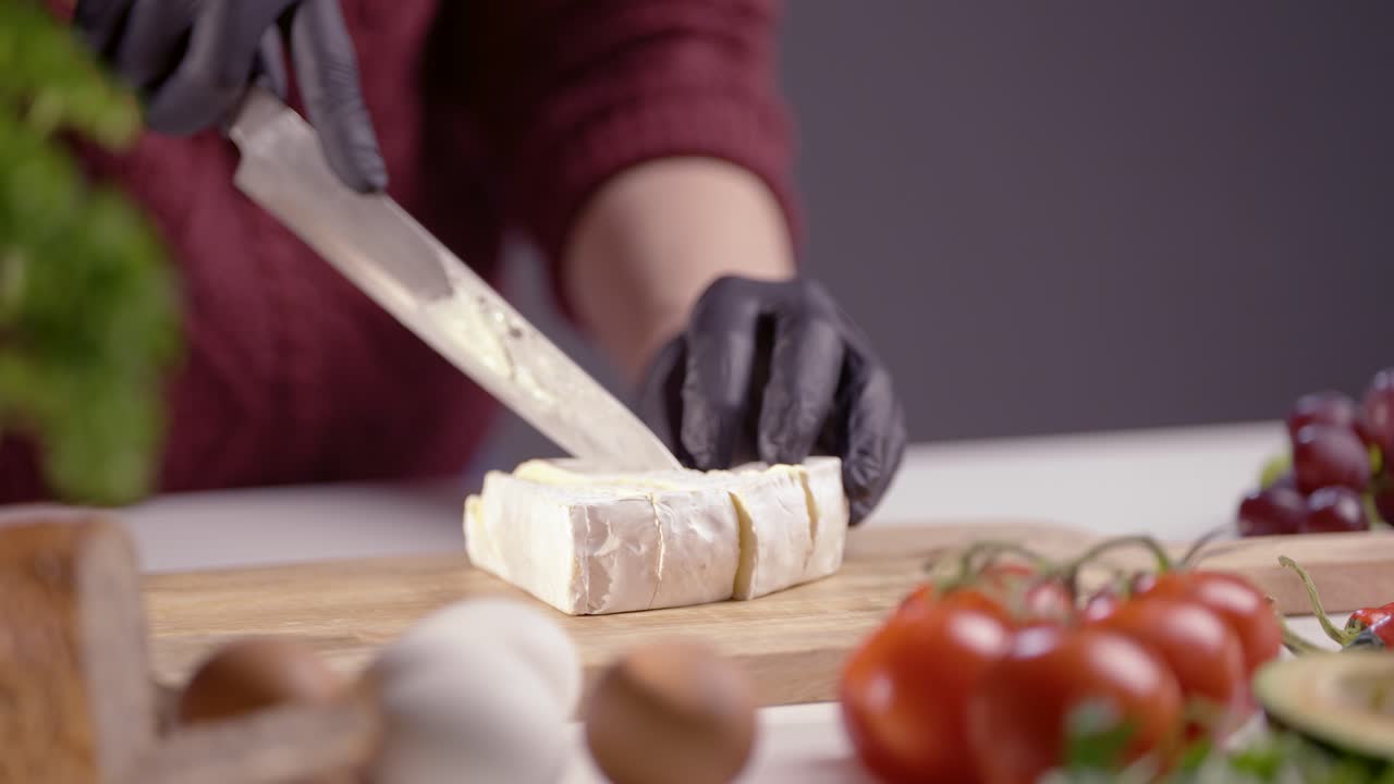 A chef skillfully slices creamy Brie cheese on a wooden board. The soft texture contrasts with the sharp blade, creating a perfect gourmet preparation. Fresh food ingredients