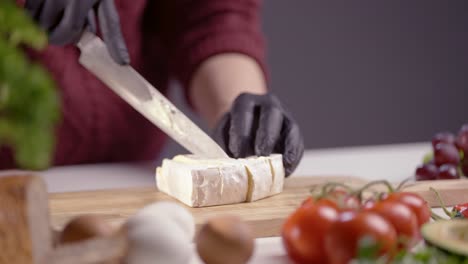 a chef skillfully slices creamy brie cheese on a wooden board. the soft texture contrasts with the sharp blade, creating a perfect gourmet preparation. fresh food ingredients