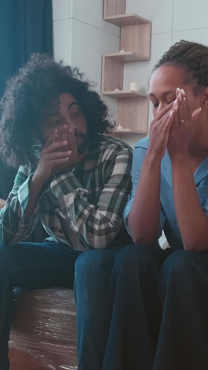 Young tired woman and man sit on sofa and exhaustedly touch faces after move