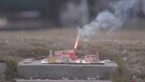 a christmas ginger bread and graham cracker decoration has a large fire cracker or m 80 being lit on it by a flame from a blow torch