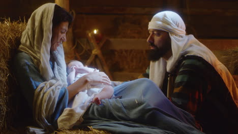 mary and joseph with baby jesus resting in dim barn. mother mary and saint joseph with baby resting after son of god birth in dark stable on christmas day in bethlehem. vertical shot