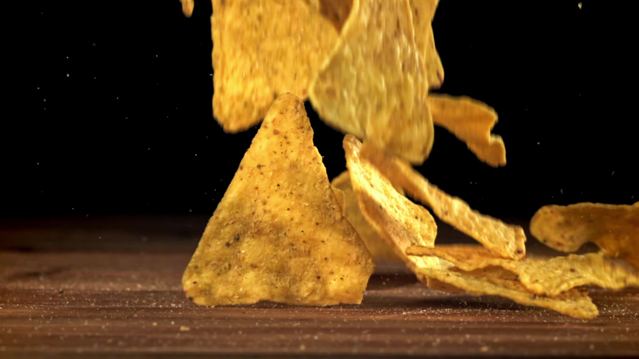 Slow motion av kryddade tortillachips som faller ner på ett träbord