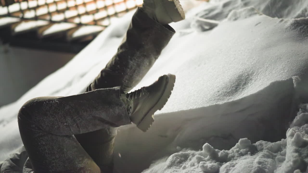 Female dancer lying on snowy ground kicking legs gently while swaying to music under street lights in winter park at night capturing artistic movement, playful mood and ambient glow in park scene