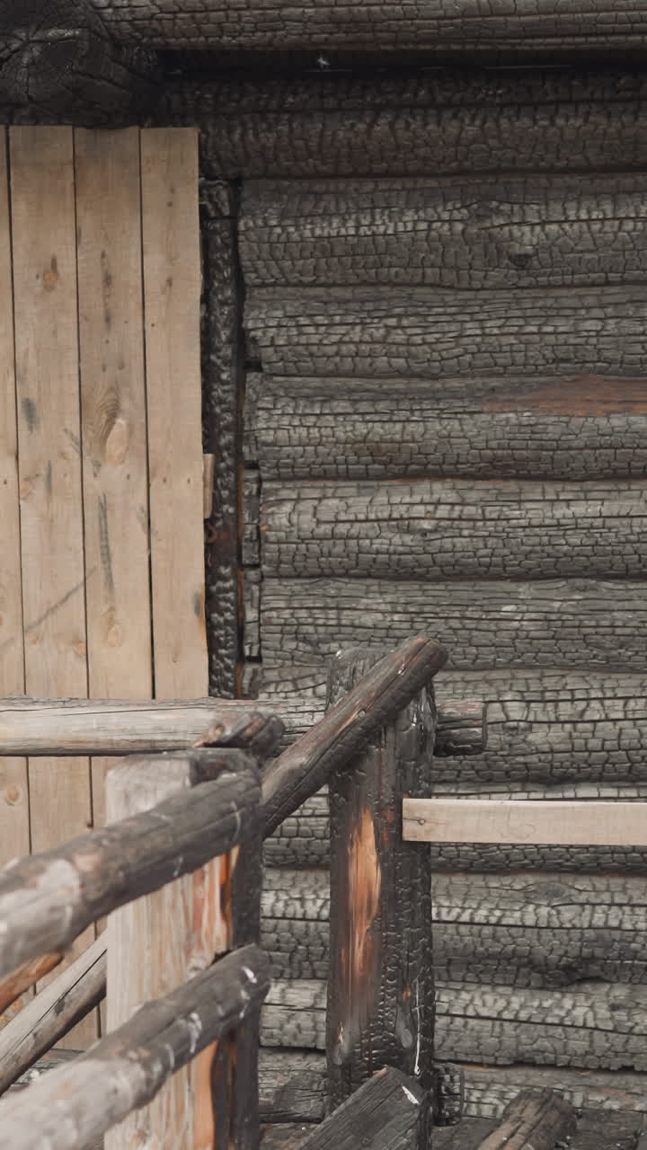 antigua cabaña de madera con puerta de entrada en el porche. escaleras de madera con plataforma y barandillas. casa de estilo tradicional construida con troncos quemados. arquitectura medieval