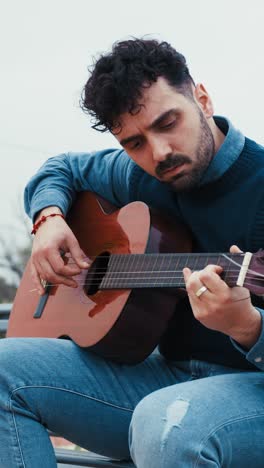 man relaxes on a bench playing the guitar outdoors