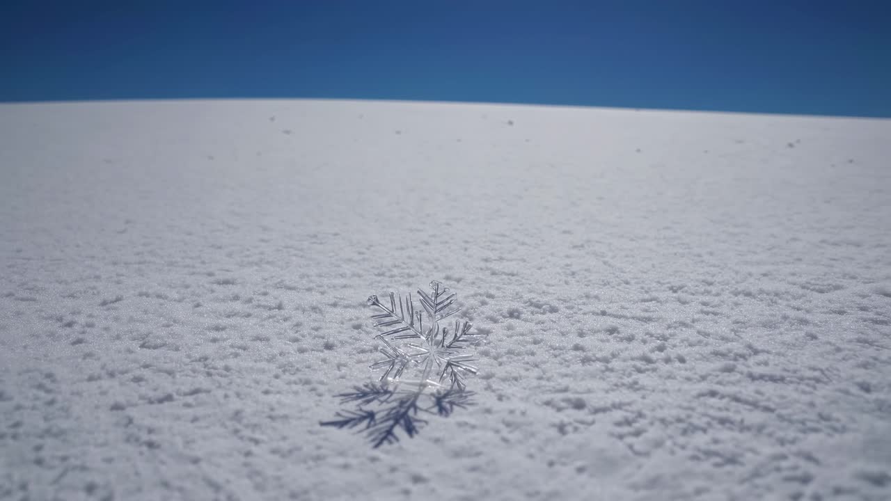 Low-angle shot of a snowflake on a vast snowy landscape under a clear blue sky, capturing a serene