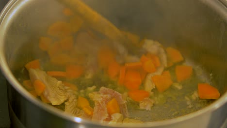 the cook mixes chicken and fresh cut carrots in the steel pot, making pasta salad, handheld close up shot