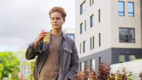 young man with earphones drinking coffee in city