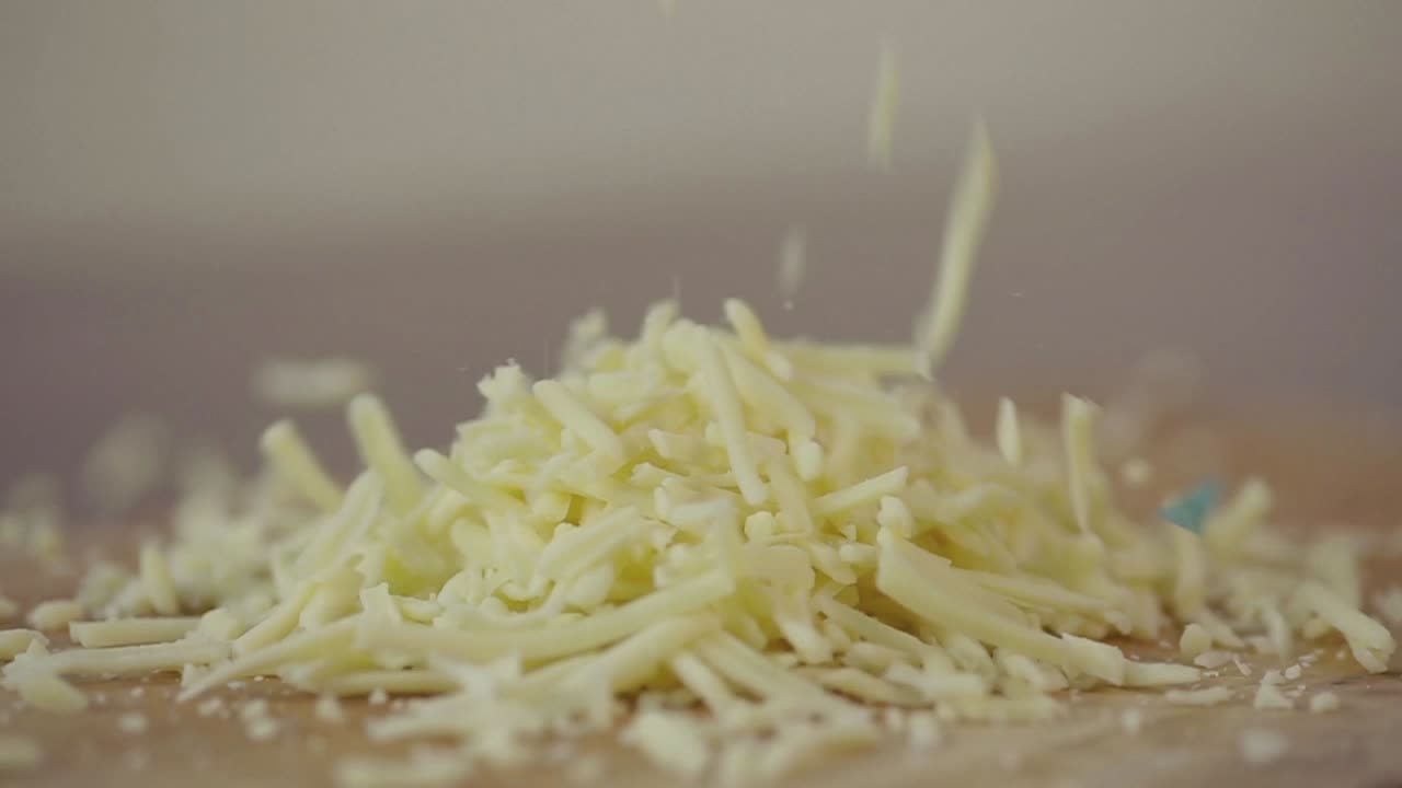 Formaggio grattugiato che cade su un tagliere di legno al rallentatore