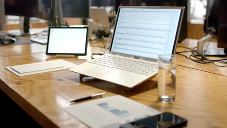 a modern business laptop open on a spreadsheet dominates a wooden office desk