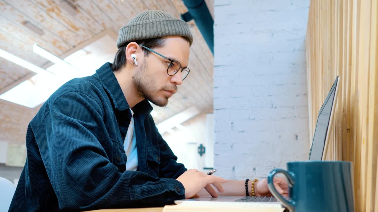 안경을 쓴 프로그래머는 노트북에서 일하고 차나 커피를 마시며 편안한 사무실을 운영합니다.