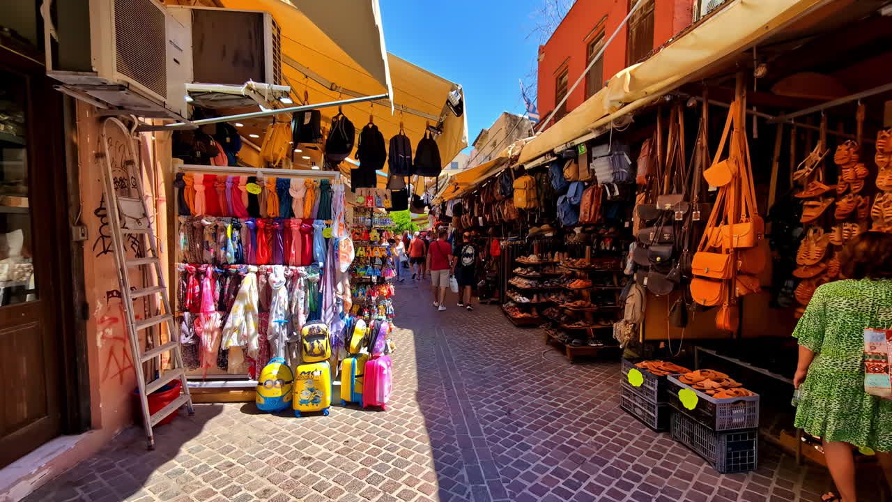 Pathway through market stalls selling bags, shoes, trinkets, bustling scene