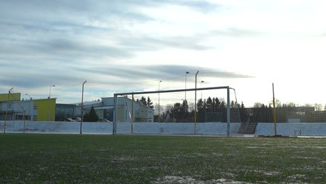 low angle footage of a soccer stadium field or a green football field during winter time when soccer goal is visible. the green grass is slightly covered in snow during winter sunny and cloudy day.