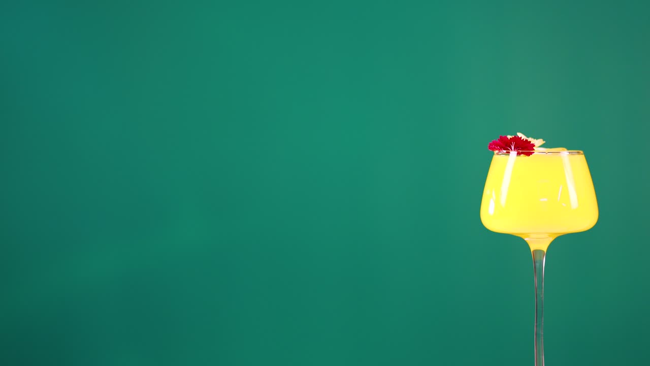 A vibrant yellow cocktail with floral garnish against a green screen backdrop, showcasing minimal movement and bright lighting
