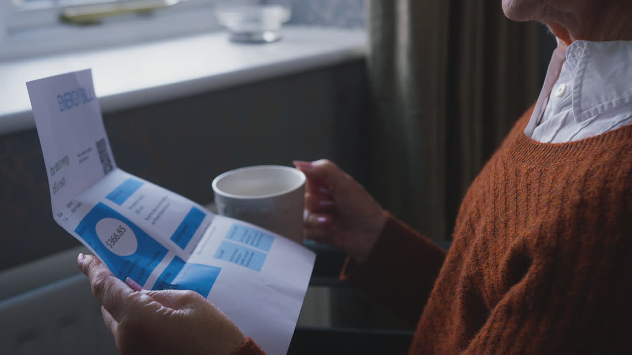 Ældre kvinde i kørestol med amerikansk energiregning ved radiator midt i leveomkostnings- og energikrisen.