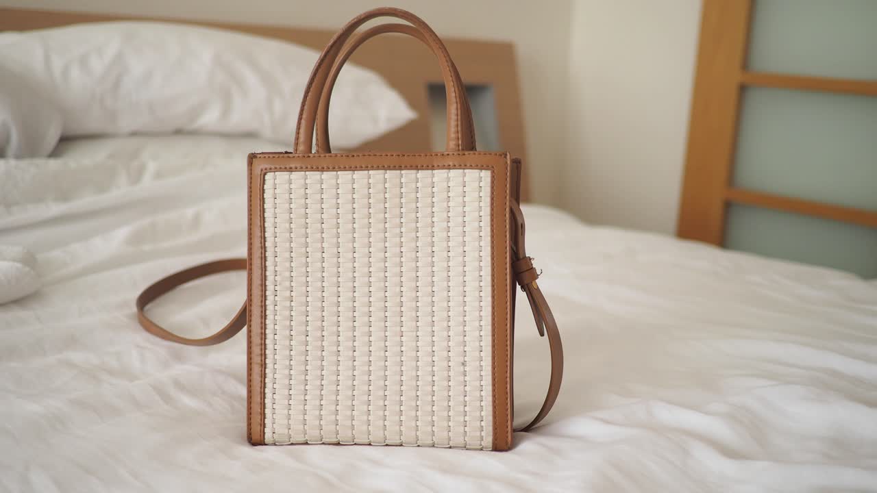 Elegante borsa a mano intrecciata con dettagli in pelle marrone su un letto.
