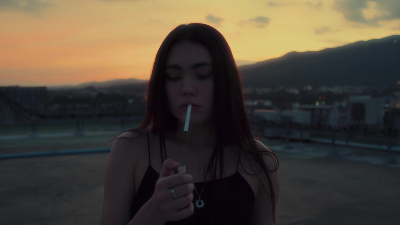 Giovane donna che fuma una sigaretta sul tetto al tramonto