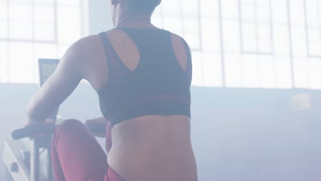 sección media de una mujer afroamericana entrenando en una máquina de remo en el gimnasio, en cámara lenta