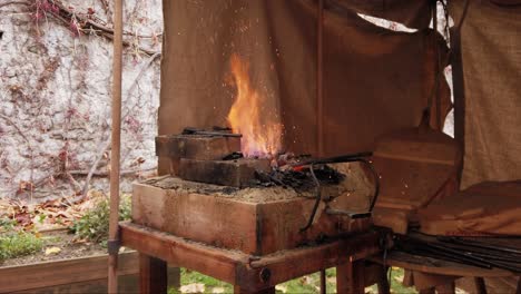 close shot of blowers stoking a brick forge fire, rural fabric cabin, blow ashes