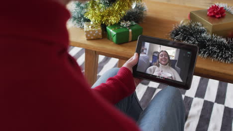 hombre caucásico agitando y usando una tableta para una videollamada de navidad con una mujer sonriente en la pantalla