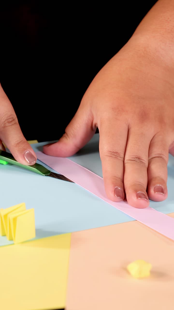 Primo piano di mani che tagliano carta rosa con un taglierino
