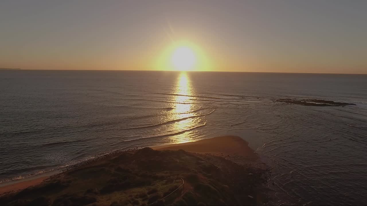 cámara moviéndose de derecha a izquierda con el amanecer en el centro del encuadre escaneando el agua y el paisaje
