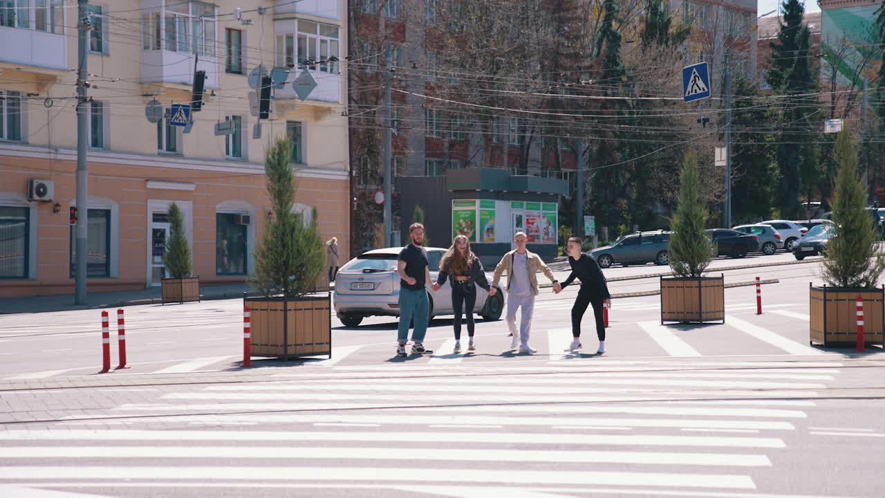 Teenagers in the city street in sunny day. Young people jumping together holding hands on the urban background near the road. Happy friends outdoors.