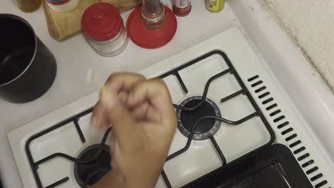 hand strikes a match to light a gas stove burner in a kitchen environment.