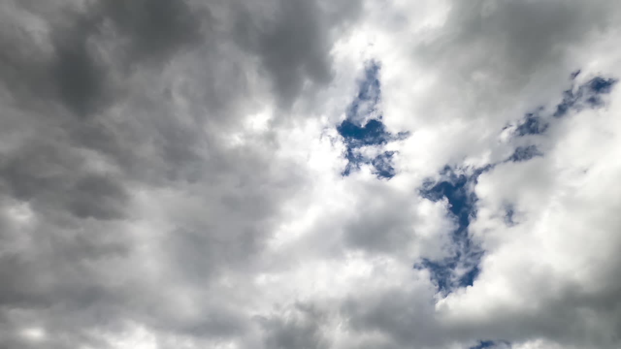 Grey clouds covering the blue sky totally. Bright sun breaking through the cloudscape. Timelapse.