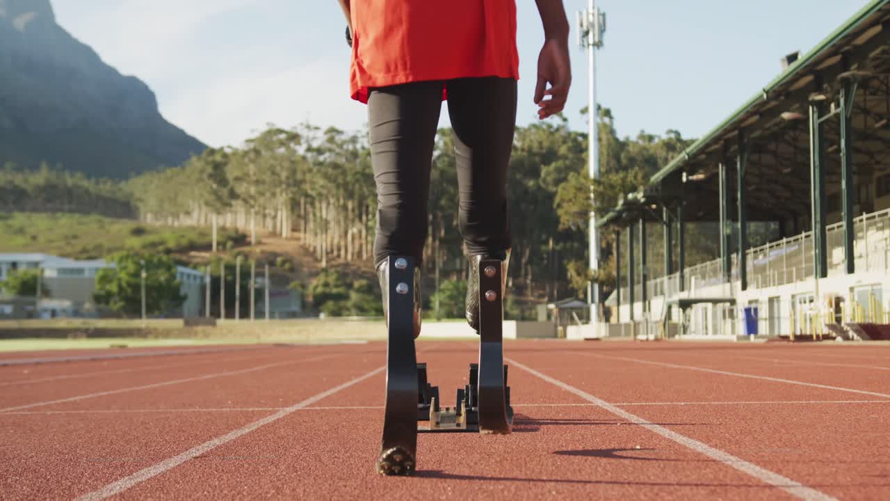 Disabled mixed race man with prosthetic legs walking on racing track towards starting blocks