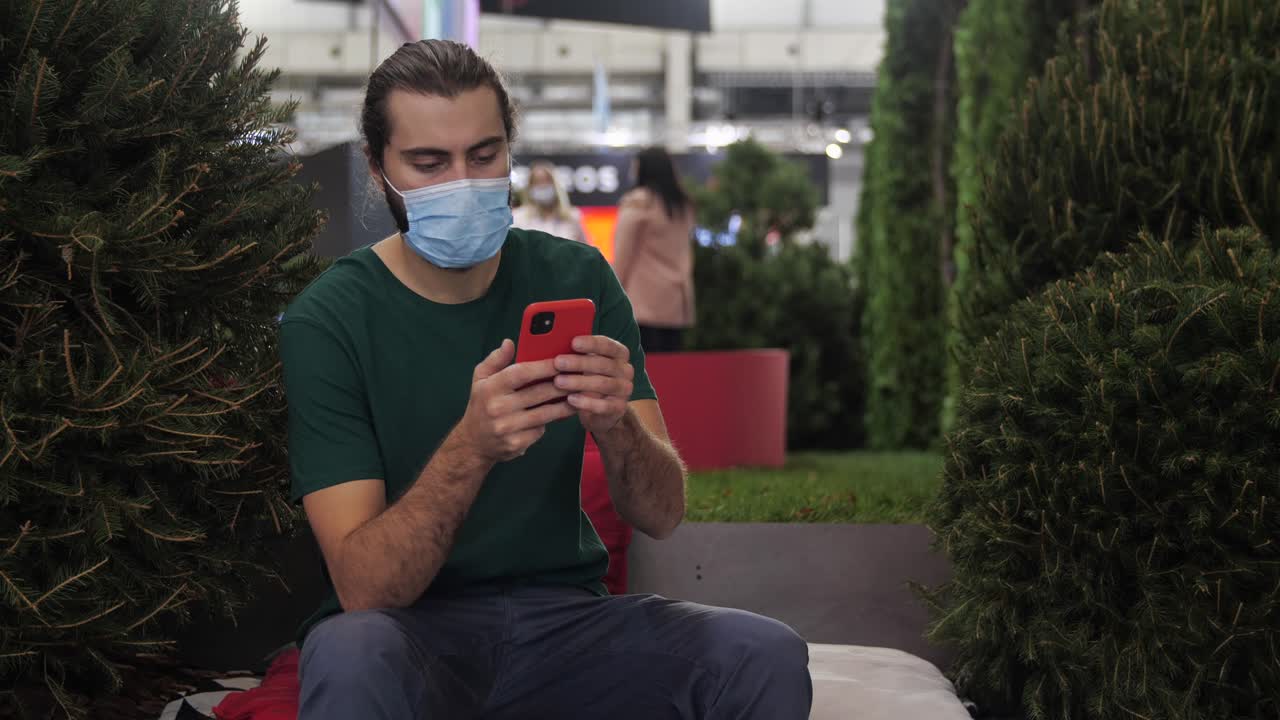 hombre usando un teléfono inteligente en un evento indoor, usando una máscara facial