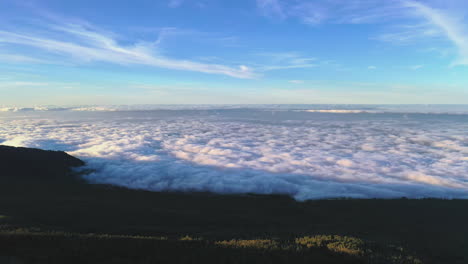 view on a dense cloud inversion below the hillside of the pico de teide mountain on canary island lit by the evening sun and a blue sky above