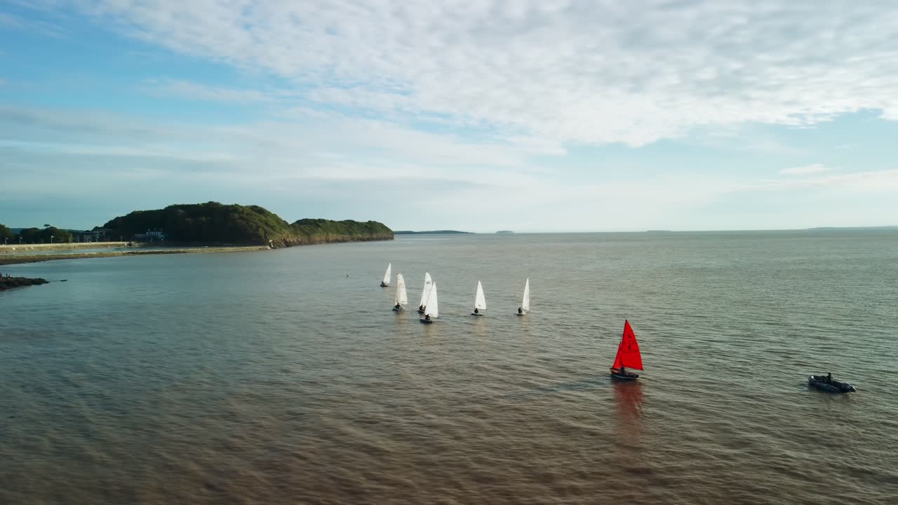 Una ripresa con drone di piccole barche a vela al largo della costa di Clevedon, Regno Unito. La ripresa panoramica si sposta a destra per rivelare il tramonto.