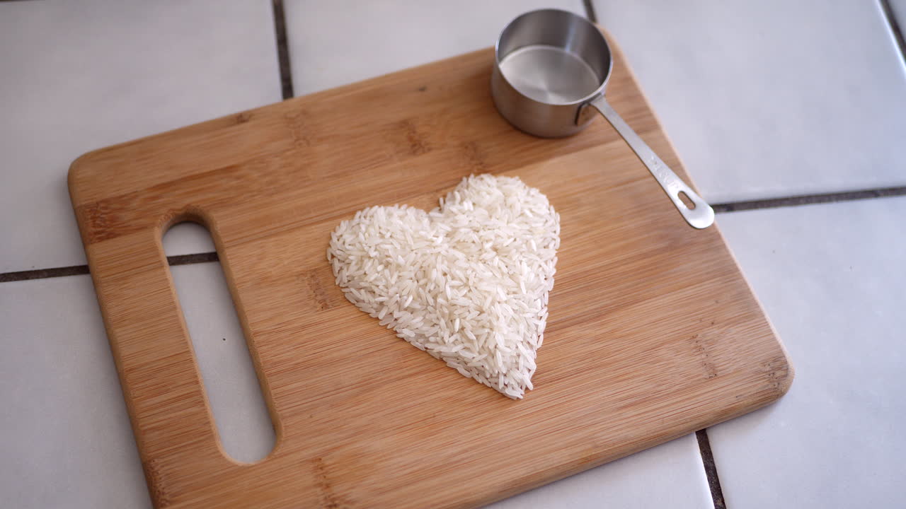 grano de arroz blanco en un corazón con utensilios de cocina y una taza medidora en una diapositiva de cocina a la derecha