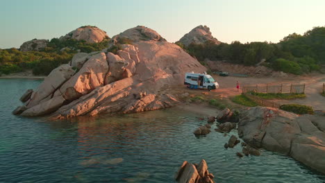 Weißer-Lieferwagen,-Geparkt-An-Einem-Wunderschönen-Ort-Am-Meer-Mit-Blauem,-Ruhigem-Wasser,-Felsen-Und-Grüner-Vegetation-Im-Hintergrund