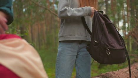 close-up of siblings walking through a serene forest, carrying backpacks as they prepare for a break, the young woman in a gray sweater carefully lowers her backpack, unzipping the bag